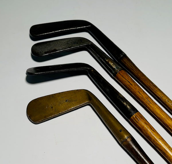 Four-piece gutty-era hickory golf play set with three smooth-face irons and a brass putter on a white background - Featured Image