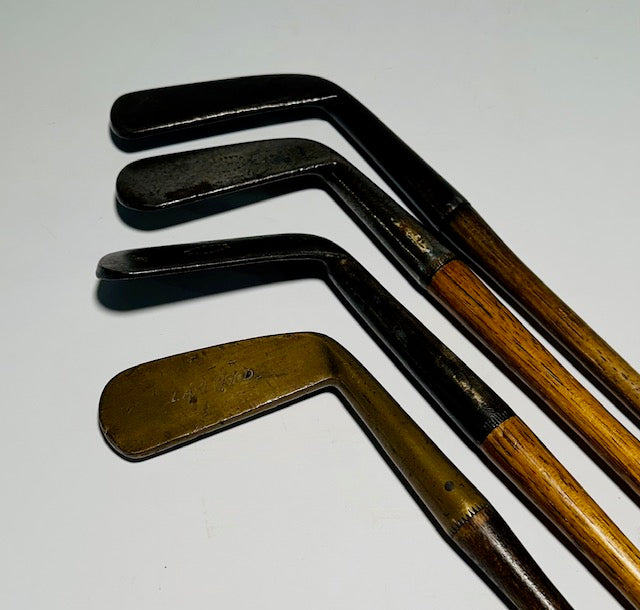 Four-piece gutty-era hickory golf play set with three smooth-face irons and a brass putter on a white background